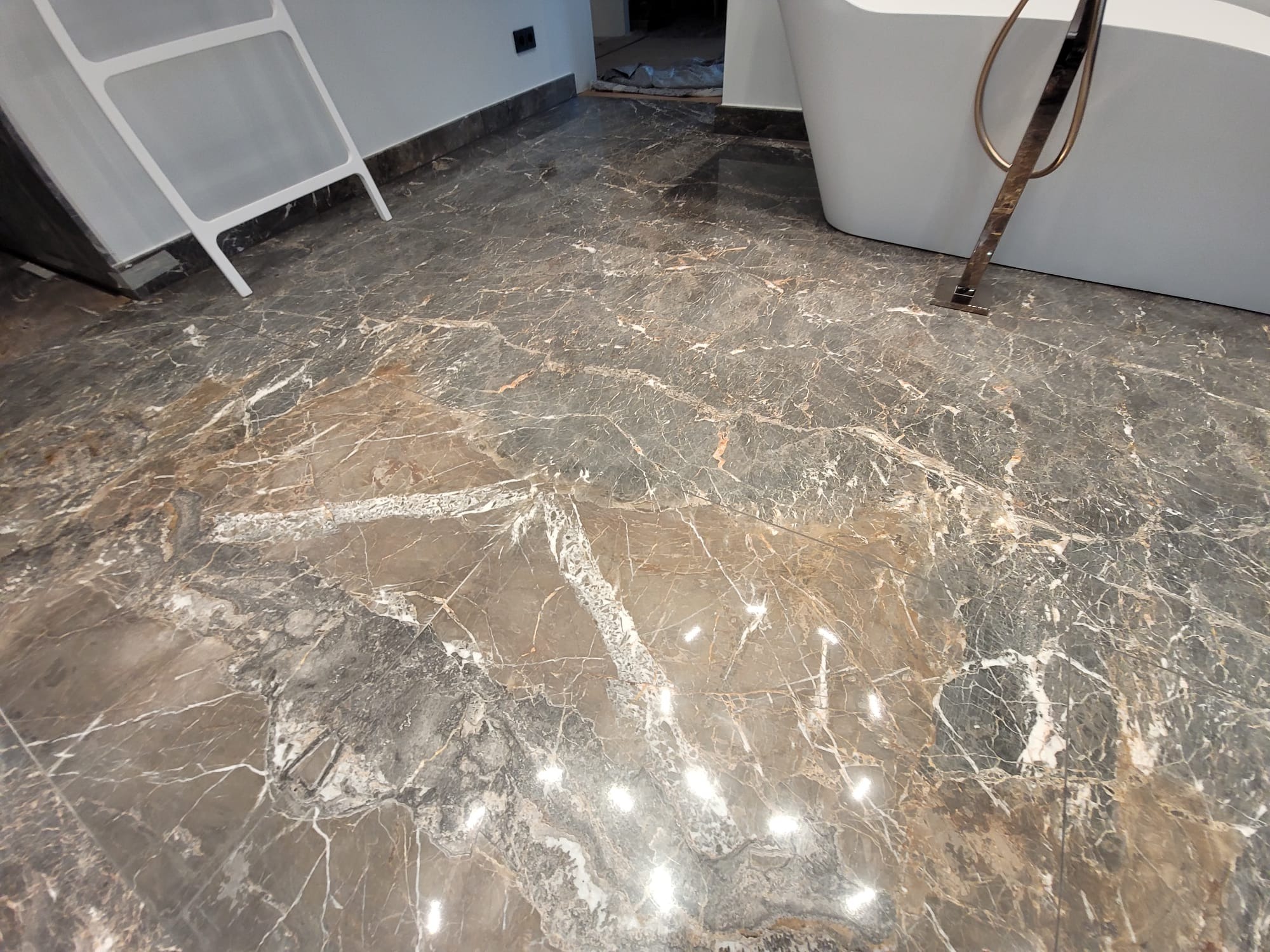 Połyskująca, marmurowa podłoga w łazience z wanną i drabinką. Ciemny marmur z jasnymi żyłami tworzy elegancki wzór. Widoczne detale wykończenia.