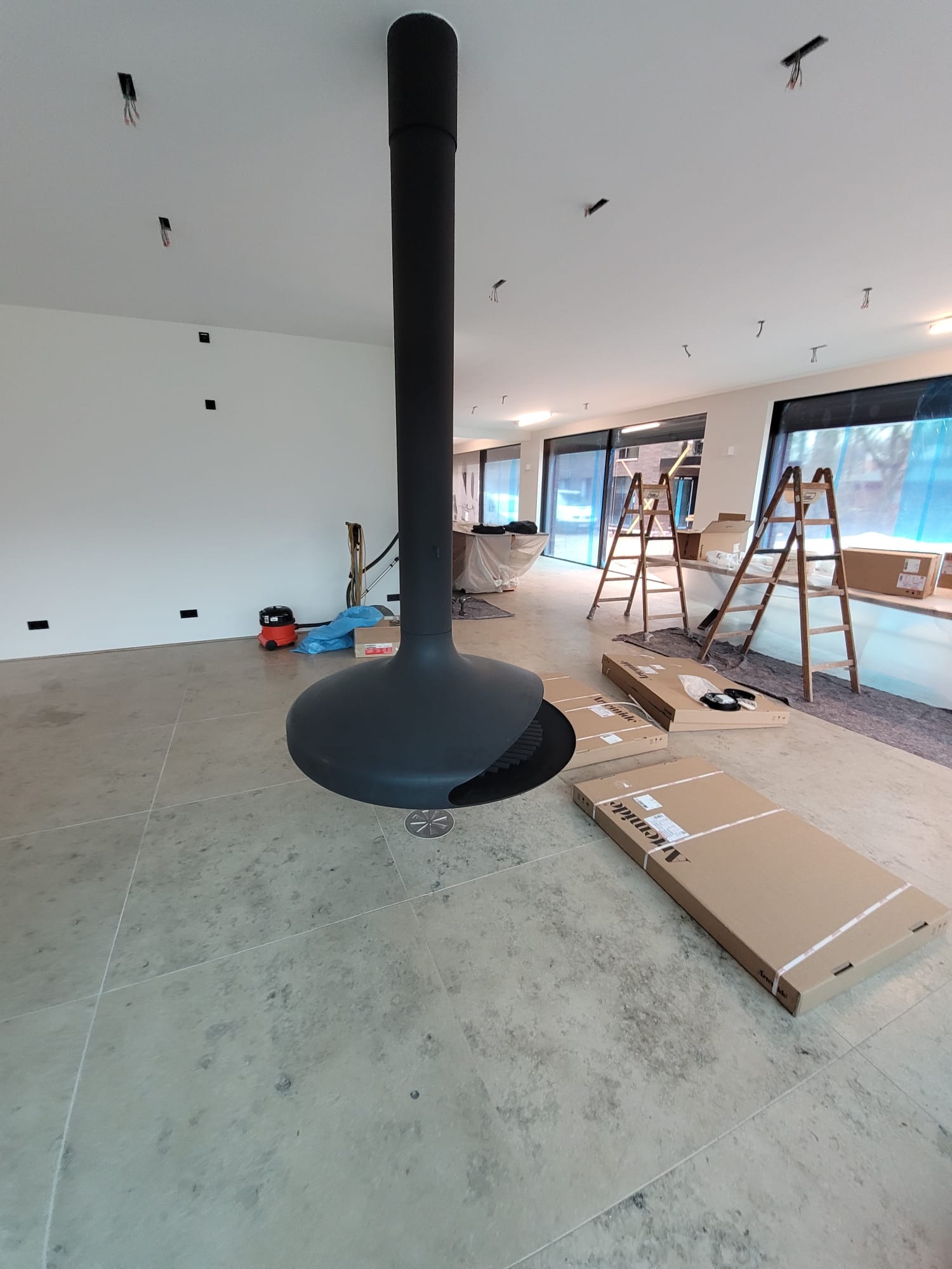 Wnętrze w trakcie wykończenia z zamontowaną, designerską lampą sufitową w kolorze czarnym. Widoczne kartony, drabiny i narzędzia.