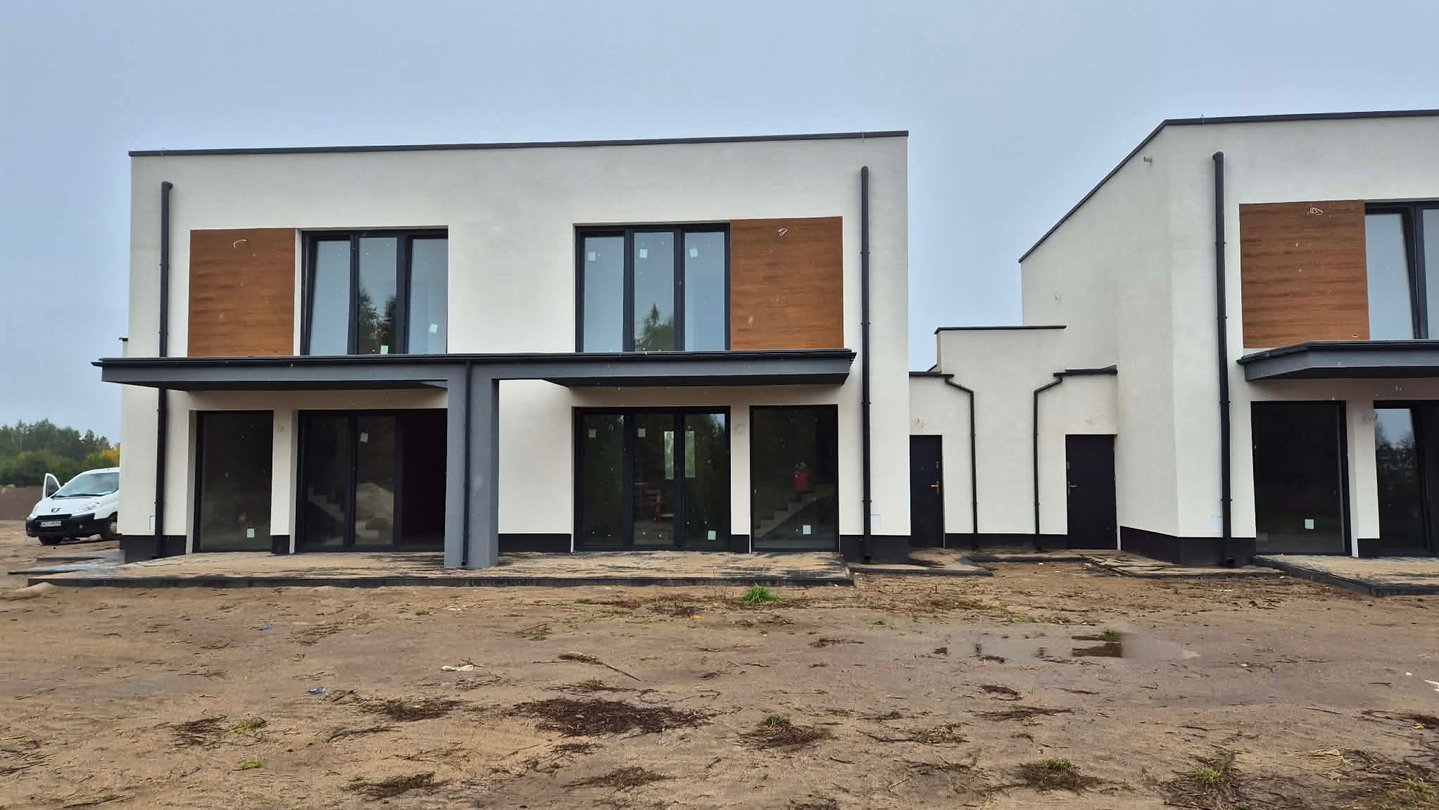 Nowoczesny dom z białą elewacją i drewnianymi panelami dekoracyjnymi. Widoczne duże okna i drzwi balkonowe. Minimalistyczny design, surowy krajobraz.