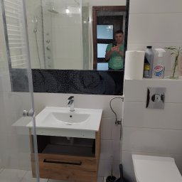 Serhii Moiseiev Renonty Poznań i Okolice - Nowoczesna łazienka z kabiną prysznicową, umywalką z szafką z drewnianym frontem i toaletą. W lustrze odbija się osoba robiąca zdjęcie.
