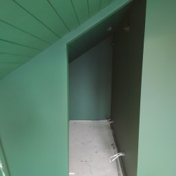 Serhii Moiseiev Renonty Poznań i Okolice - Świeżo pomalowane na zielono poddasze ze skośnym sufitem i wejściem do garderoby. Widoczne ślady farby na podłodze i narzędzia malarskie.
