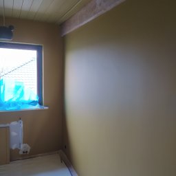 Serhii Moiseiev Renonty Poznań i Okolice - Pokój po gładzi w odcieniach beżu, zabezpieczone okno i podłoga, widoczny fragment sufitu z drewnianymi belkami w Poznaniu. Przygotowanie do dalszych prac.