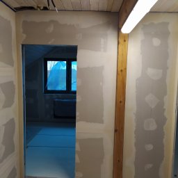 Serhii Moiseiev Renonty Poznań i Okolice - Wnętrze w trakcie prac wykończeniowych: ściany z nałożoną gładzią, drewniana boazeria na suficie, widoczne kable i oświetlenie. Przygotowanie do malowania.