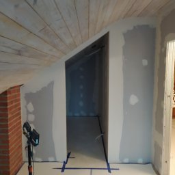 Serhii Moiseiev Renonty Poznań i Okolice - Poddasze w trakcie gładzi: ściany przygotowane, sufit z desek, oświetlenie robocze. Widoczne ślady po łataniu i szpachlowaniu. Taśmy malarskie na podłodze.