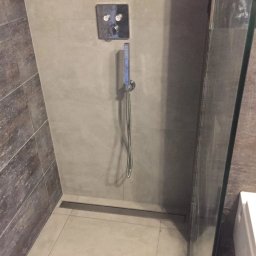 Serhii Moiseiev Renonty Poznań i Okolice - Nowoczesna kabina prysznicowa z odpływem liniowym, szara armatura i płytki w odcieniach beżu i brązu. Minimalistyczny design, widoczne szklane drzwi.