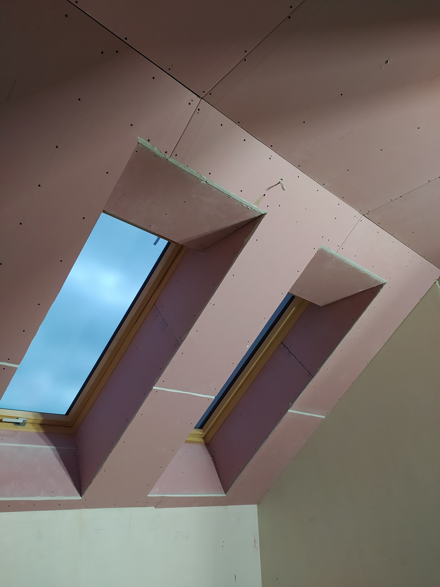 Płyty gipsowo-kartonowe zamontowane na poddaszu, widoczne dwa okna dachowe. Etap przygotowania do dalszych prac wykończeniowych. Widok z dołu.