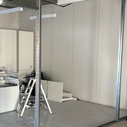 Arkadiusz Burzyński - Montaż ścianki działowej z profili metalowych w biurze. Widoczne kable, drabina i elementy wyposażenia. Podłoże przygotowane pod układanie płytek.