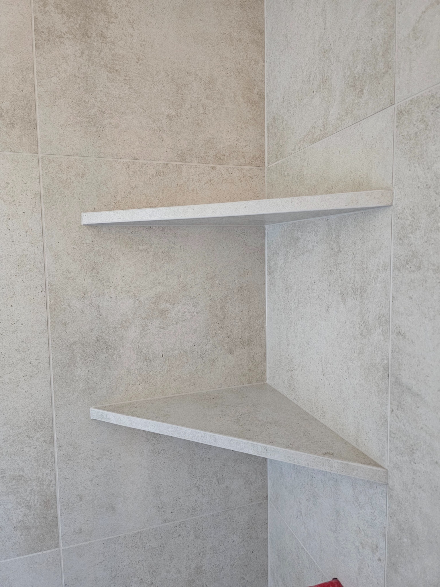Narożne półki z płytek w kabinie prysznicowej, wykończone w jasnych, beżowych odcieniach. Minimalistyczny design, precyzyjne wykonanie, widoczne fugi.