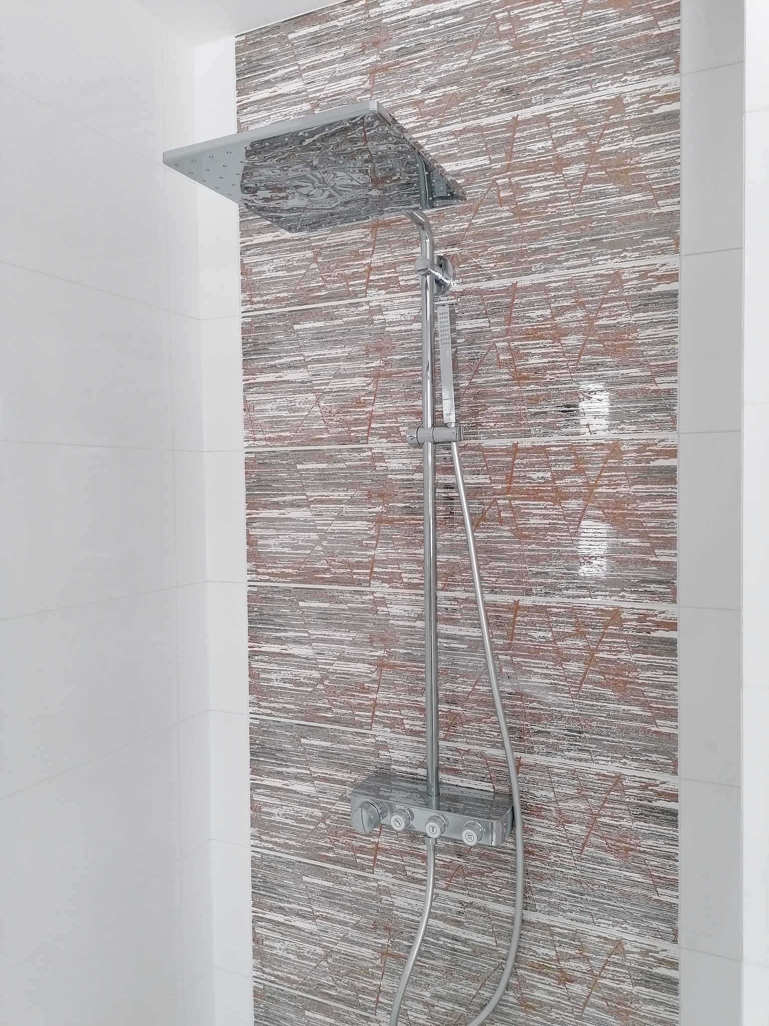 Nowoczesny panel prysznicowy z deszczownicą na tle ściany wyłożonej płytkami imitującymi drewno w łazience z białymi płytkami. Chromowana armatura.