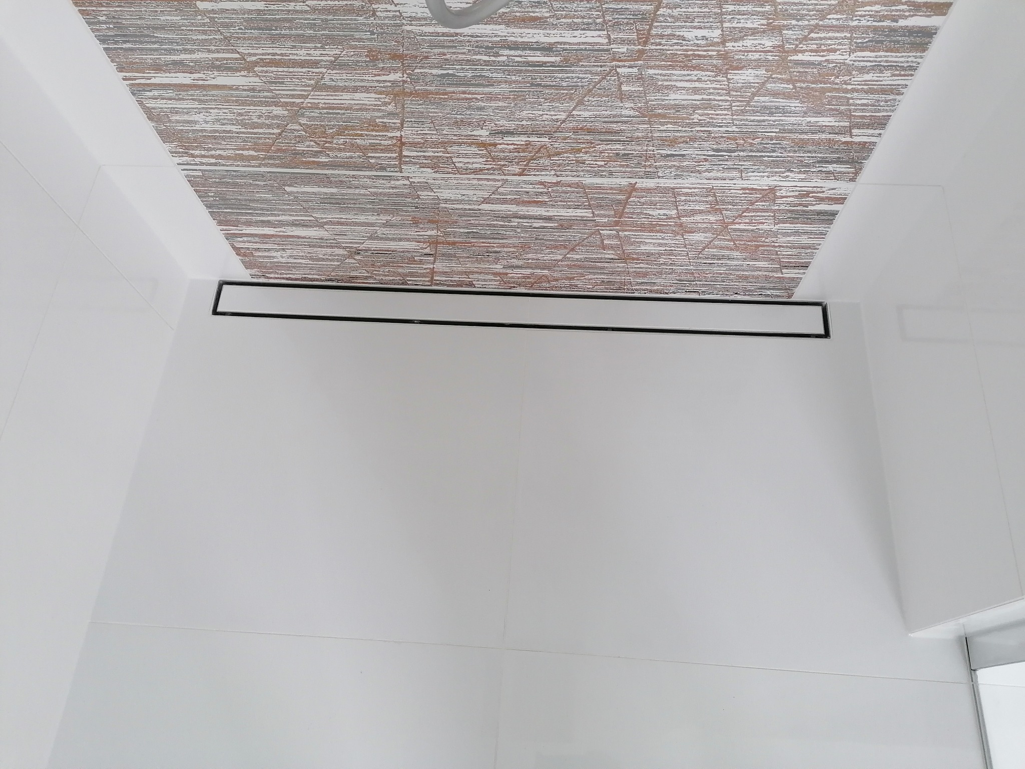 Nowoczesna kabina prysznicowa z odpływem liniowym i dekoracyjną mozaiką na suficie. Minimalistyczny design, białe płytki, czarny odpływ.