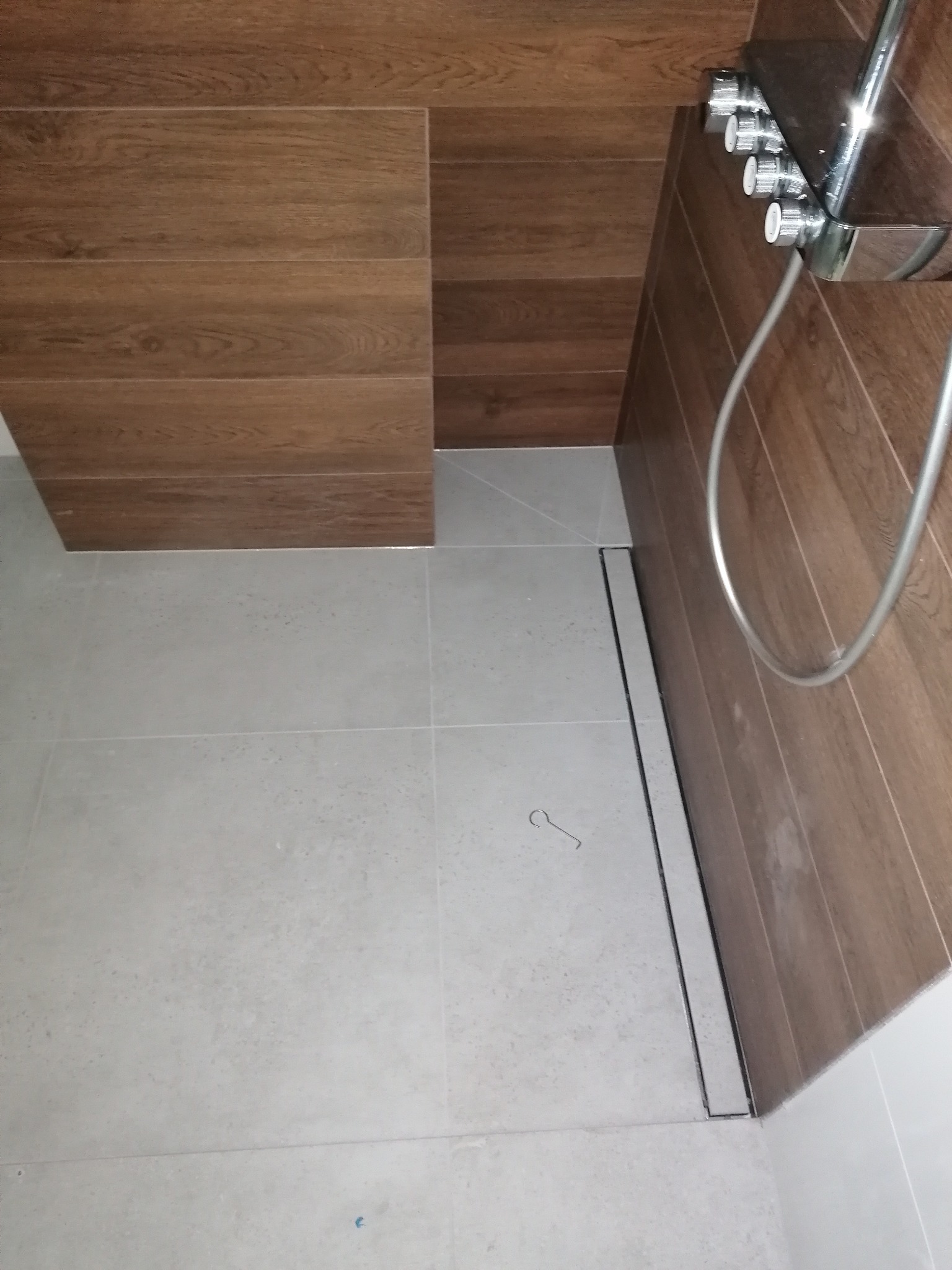 Nowoczesna kabina prysznicowa z odpływem liniowym i brązowymi płytkami imitującymi drewno na ścianach. Jasne płytki podłogowe. Minimalistyczny design.