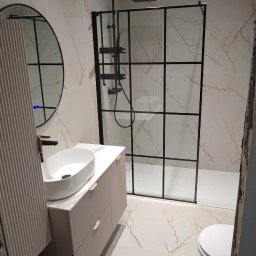 entreprise - Wykończona łazienka z kabiną typu walk-in, umywalką nablatową i okrągłym lustrem. Płytki imitujące marmur na ścianach i podłodze. Nowoczesny design.