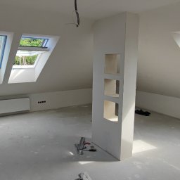 entreprise - Poddasze po szpachlowaniu i malowaniu na biało, z oknami dachowymi i wnękami w ścianie. Widoczne narzędzia malarskie i folia ochronna na podłodze.