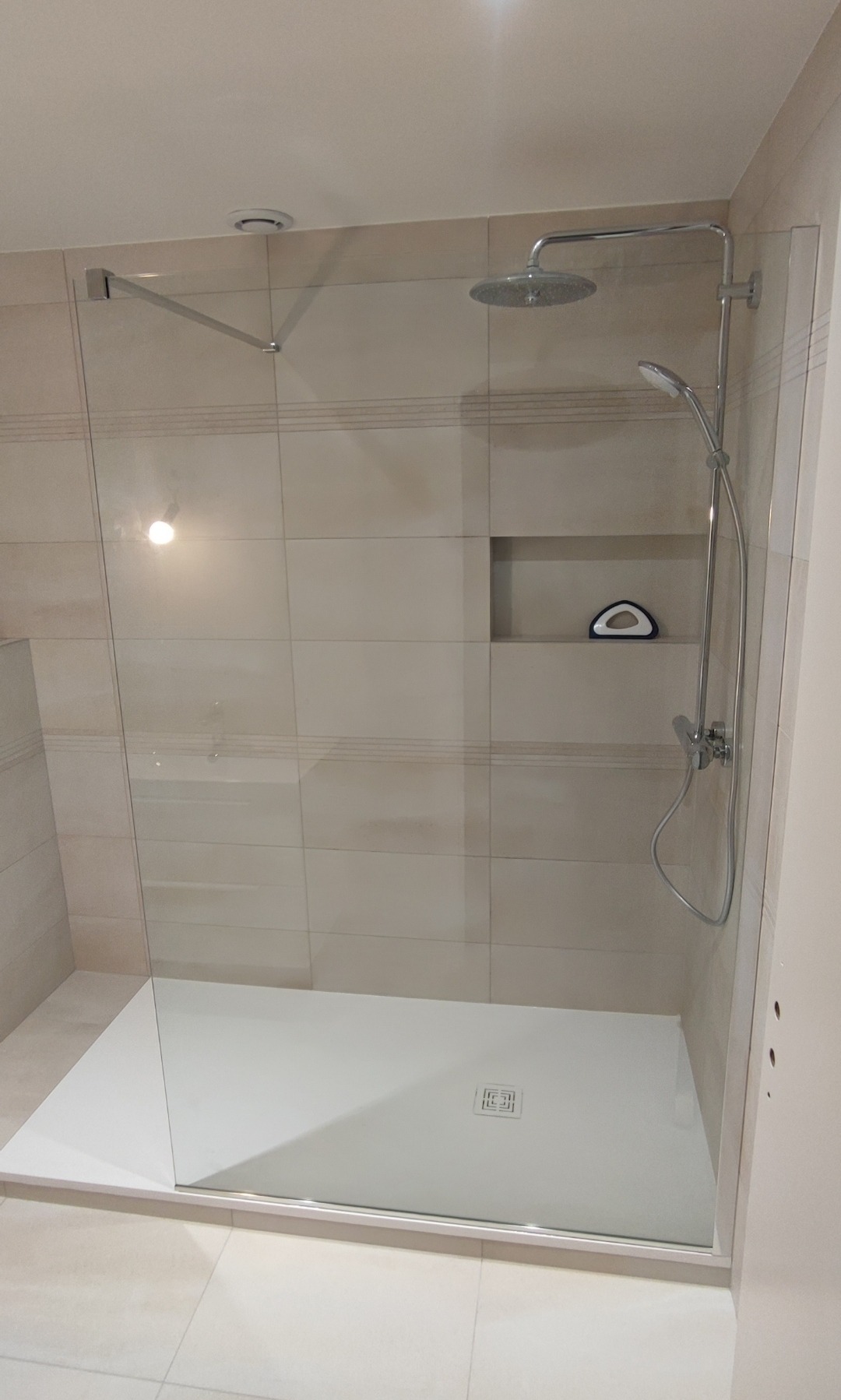 Nowoczesna kabina prysznicowa walk-in z deszczownicą i półką w ścianie, wykończona beżowymi płytkami. Minimalistyczny design, szklana ściana, biały brodzik.