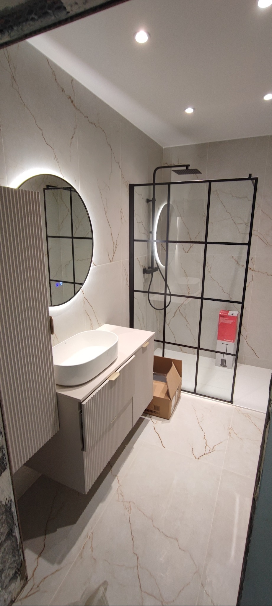 Nowoczesna łazienka z umywalką nablatową, lustrem z podświetleniem LED i kabiną prysznicową typu walk-in z czarnymi profilami. Marmurowe płytki na ścianach i podłodze.