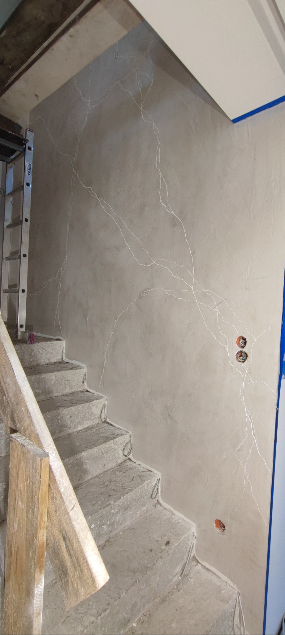 Wykończona ściana w klatce schodowej z efektem dekoracyjnym imitującym żyły kamienia. Widoczne schody w stanie surowym i drabina Krause.