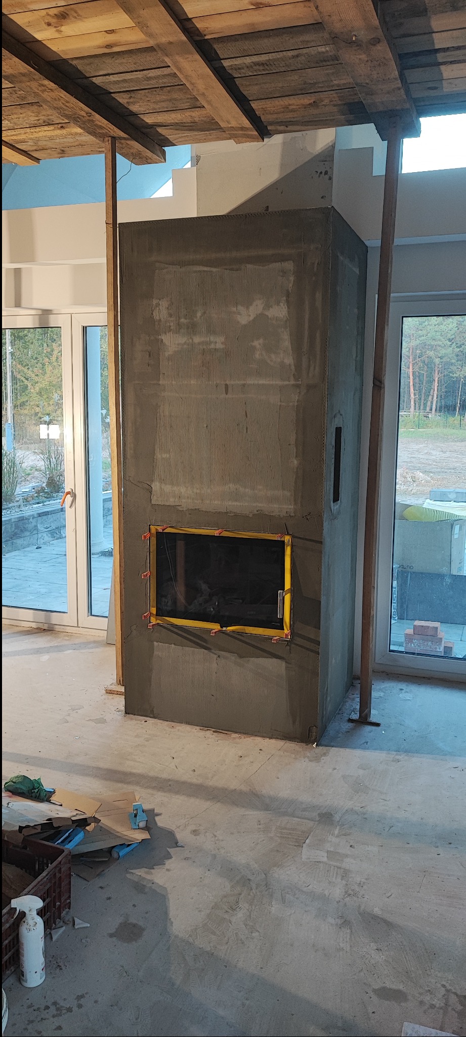 Wnętrze w trakcie budowy kominka z surowym wykończeniem, widoczne podpory i materiały budowlane. Ujęcie z bliska na kominek w stanie surowym.