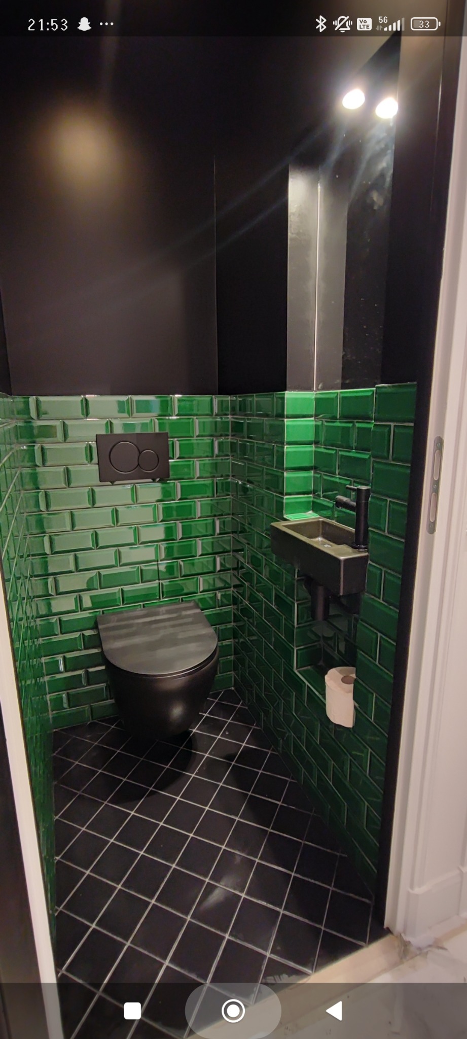 Nowoczesna toaleta: czarna armatura, zielone płytki typu metro i czarna podłoga w kratkę. Minimalistyczny design z akcentem kolorystycznym.