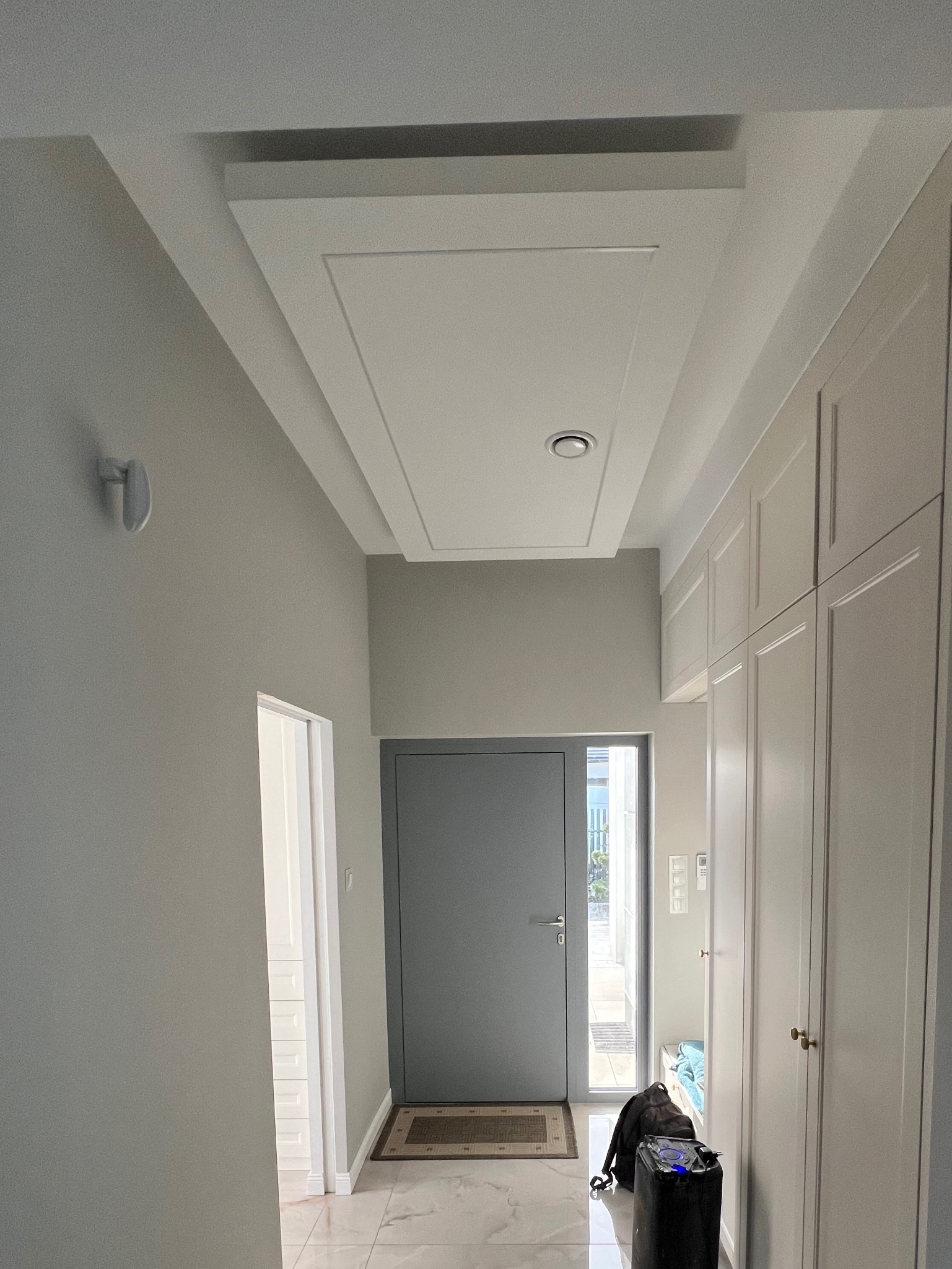 Nowoczesny przedpokój w Piekoszowie po remoncie. Białe szafy w zabudowie, szare ściany i drzwi, podwieszany sufit z oświetleniem. Eleganckie wykończenie wnętrza.