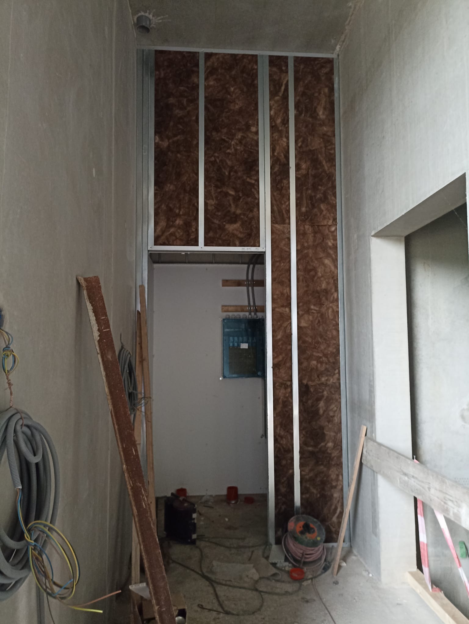 Montaż ścianki działowej z płyty karton-gips z izolacją z wełny mineralnej. Widoczne profile metalowe i instalacja elektryczna. Surowy stan wykończenia.