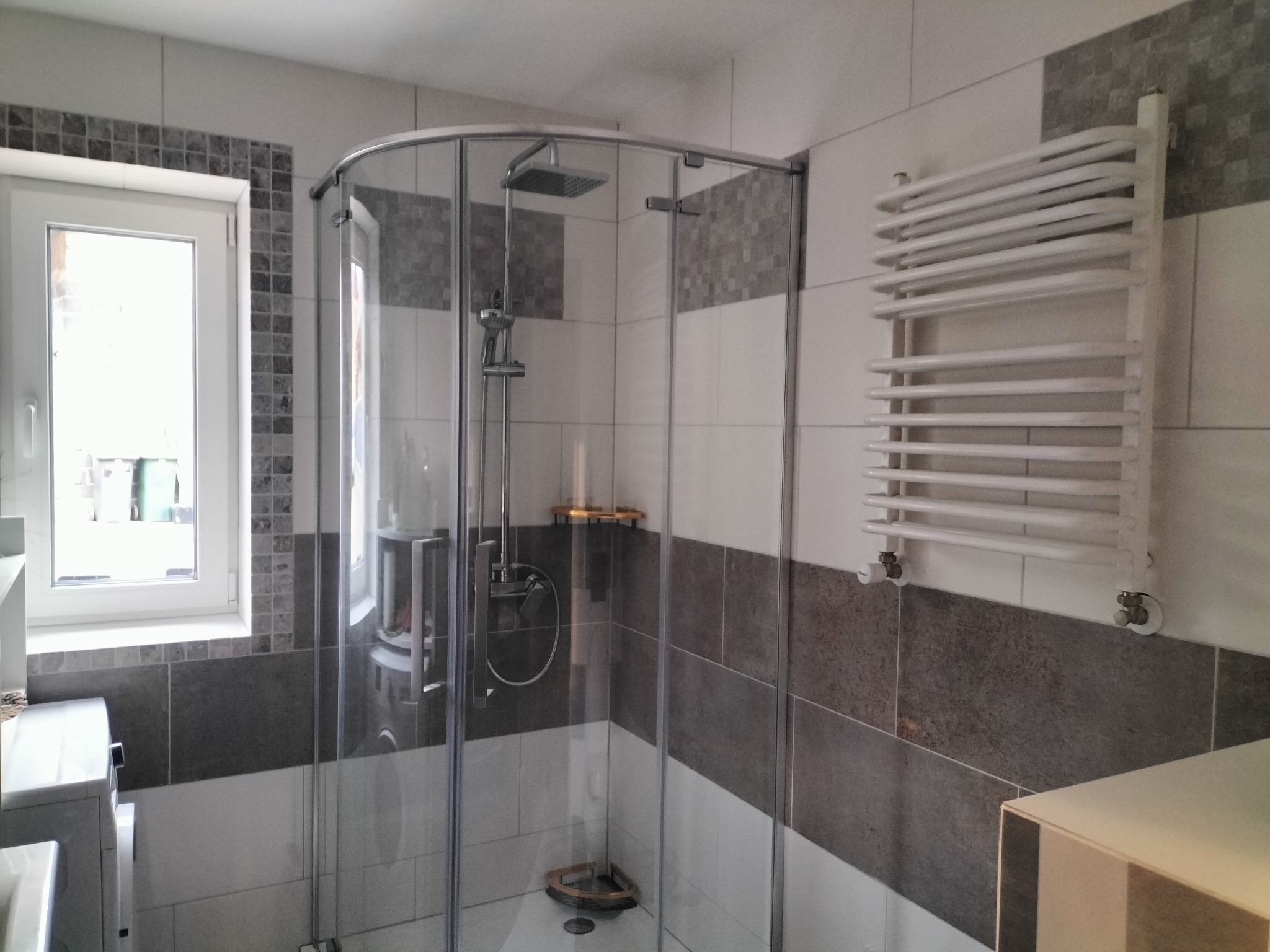 Nowoczesna kabina prysznicowa z grzejnikiem drabinkowym w wykończonej łazience w Tylmanowej. Widoczne płytki w odcieniach szarości i bieli.