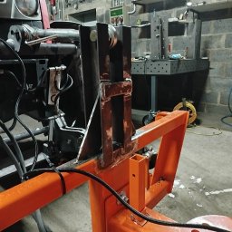 ATS Sowa - Pomarańczowa konstrukcja metalowa spawana do ciągnika w warsztacie, widoczne ślady spawania i narzędzia na ścianie z cegły.