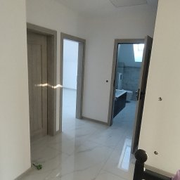 Glazura usługi ogólnobudowlane - Wykończony korytarz z marmurową podłogą i widokiem na łazienkę z wanną. Szare ramy drzwi, białe ściany i sufit z otworem rewizyjnym.