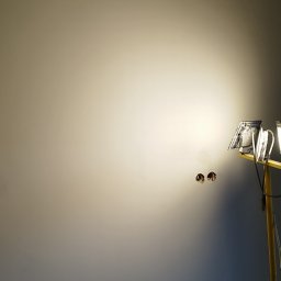 Glazura usługi ogólnobudowlane - Gładka, świeżo pomalowana ściana w odcieniach szarości, oświetlona lampą budowlaną. Widoczne puszki elektryczne. Górna krawędź ściany nierówna, surowa.