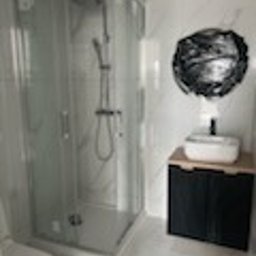 Glazura usługi ogólnobudowlane - Nowoczesna łazienka z kabiną prysznicową, umywalką nablatową na szafce z drewnianym blatem i dekoracyjnym lustrem. Białe marmurowe płytki na ścianach.