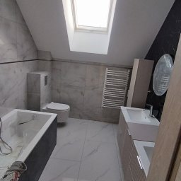 Glazura usługi ogólnobudowlane - Jasna łazienka na poddaszu z oknem dachowym. Marmurowe płytki, wanna, toaleta, grzejnik drabinkowy i szafka z umywalką. Nowoczesny design, ukończony remont.