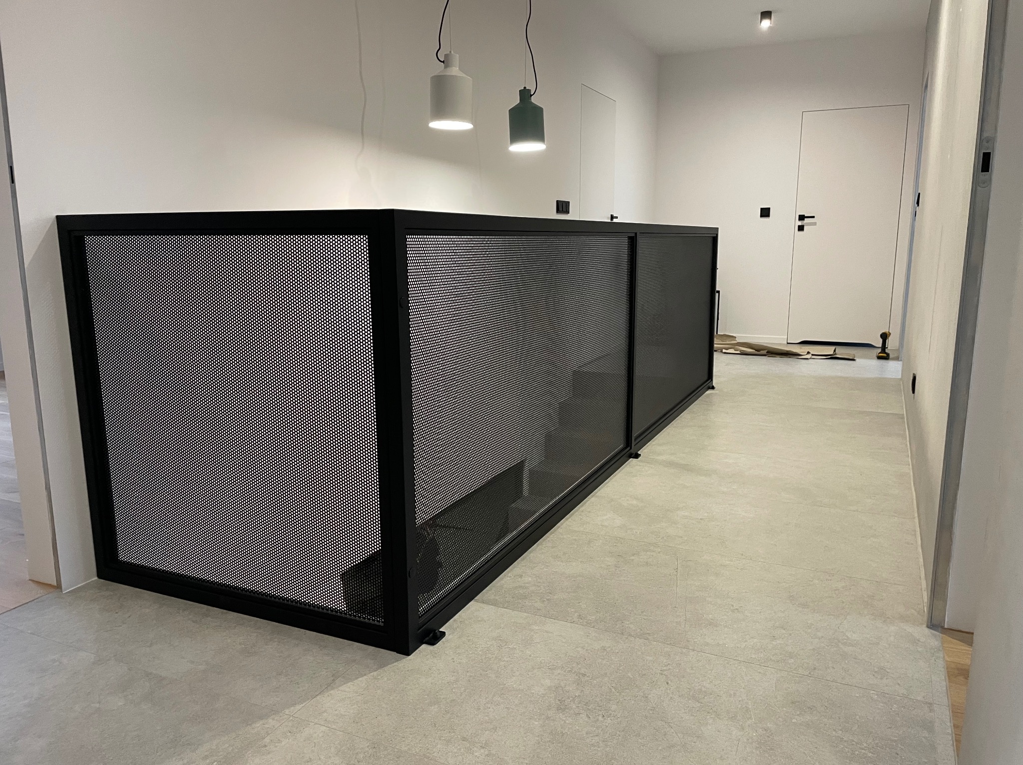 Nowoczesna, czarna balustrada metalowa z perforowanej blachy, zabezpieczająca schody w jasnym wnętrzu. Minimalistyczny design, widoczne schody i oświetlenie.