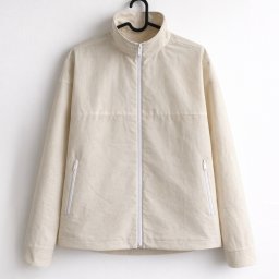 GARMENT X STUDIO - Jasnobeżowa kurtka z zamkiem błyskawicznym, wisząca na czarnym wieszaku na białym tle. Widoczne kieszenie z zamkami i stójka. Minimalistyczny design.