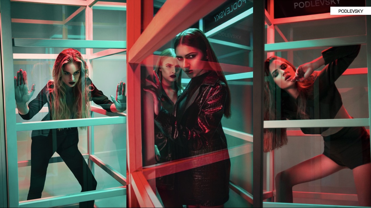 Sesja zdjęciowa z trzema modelkami w geometrycznej konstrukcji, oświetlona neonowym światłem. Ubrania w ciemnych kolorach, wyrazisty makijaż, dynamiczne pozy.