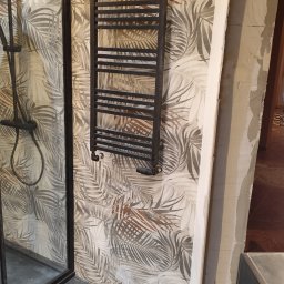 GLAZURKARZ Mateusz Moskwa - Nowoczesna łazienka z czarną kabiną prysznicową, grzejnikiem drabinkowym na ścianie w liście i ciemną podłogą. Widoczny fragment futryny drzwi.