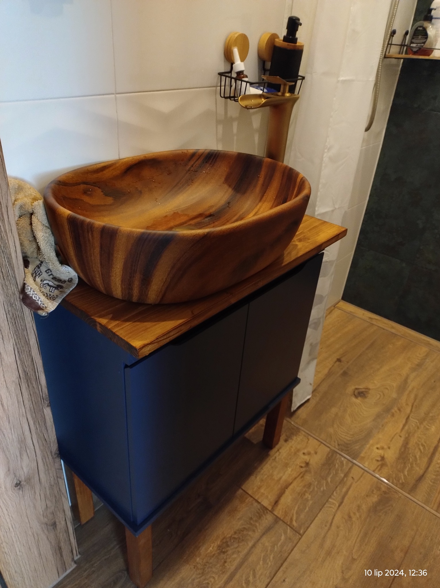 Drewniana misa umywalkowa na szafce w łazience z drewnianą podłogą. Nowoczesna armatura i akcesoria łazienkowe. Ujęcie z bliska, detale wykończenia.