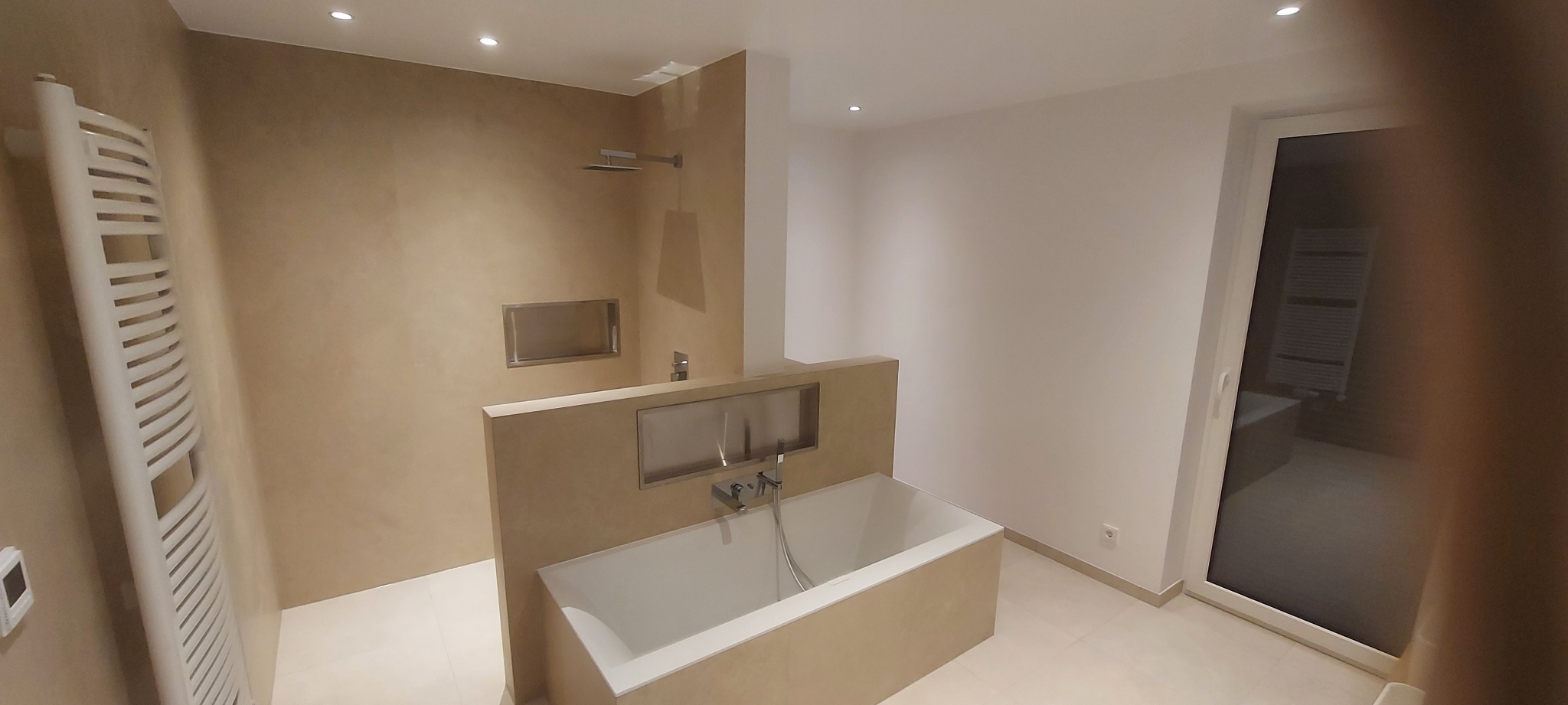 Beżowa łazienka po remoncie: wanna z zabudową, grzejnik drabinkowy, prysznic z wnęką. Minimalistyczny design, jasne płytki, nowoczesna armatura.