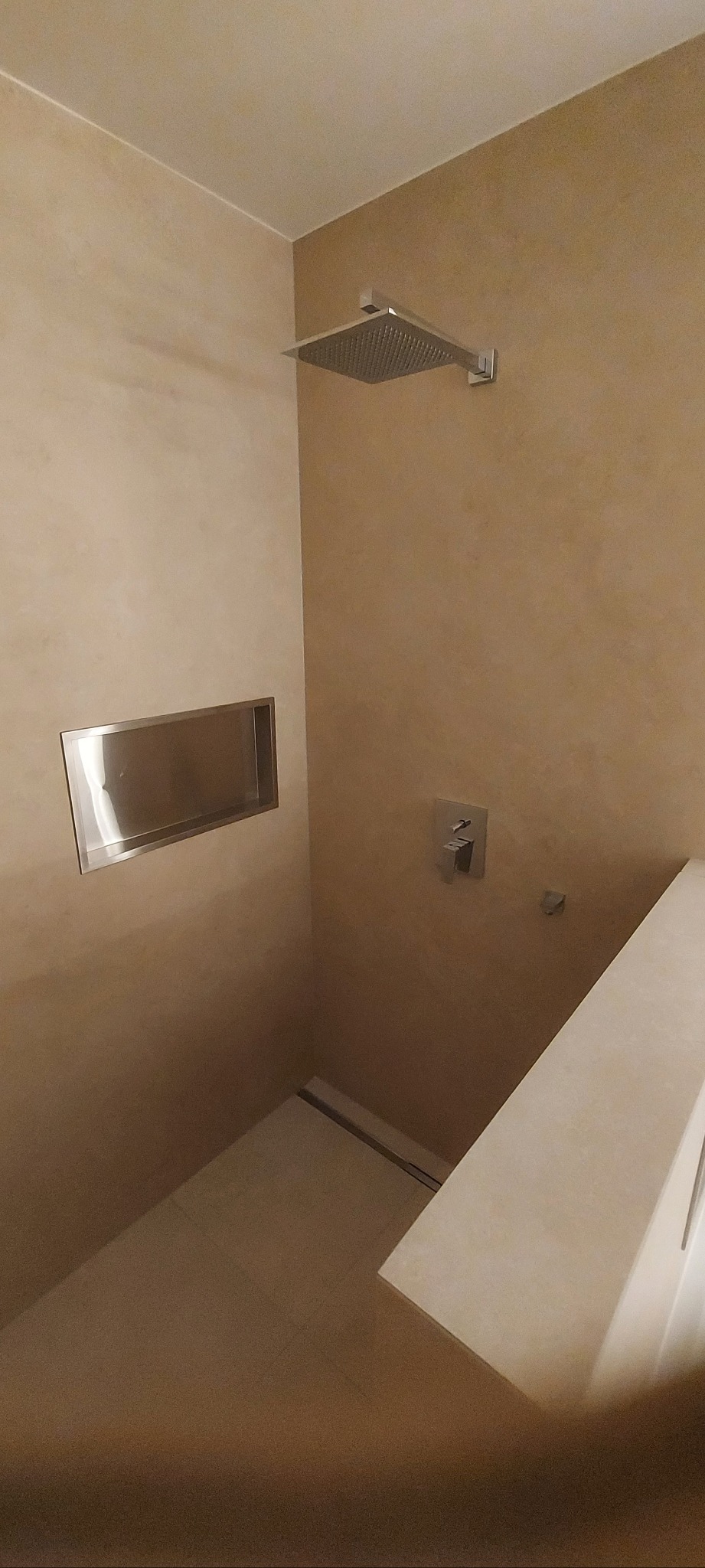 Beżowa kabina prysznicowa z kwadratową deszczownicą, wnęką na kosmetyki i odpływem liniowym. Minimalistyczny design, ciepłe oświetlenie.