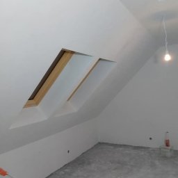 MD-BUD - Białe poddasze ze skośnymi oknami dachowymi, świeżo po malowaniu. Widoczny wałek malarski i surowa podłoga. Minimalistyczne wnętrze w trakcie wykańczania.