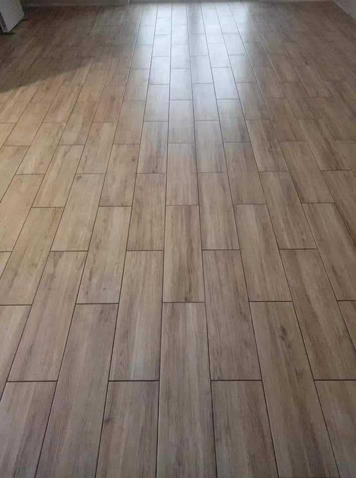 Ułożona podłoga z płytek imitujących drewno, z widocznymi fugami. Płytki ułożone w prostokątnym wzorze, z perspektywą zbiegającą się w oddali. Jasne, naturalne oświetlenie.