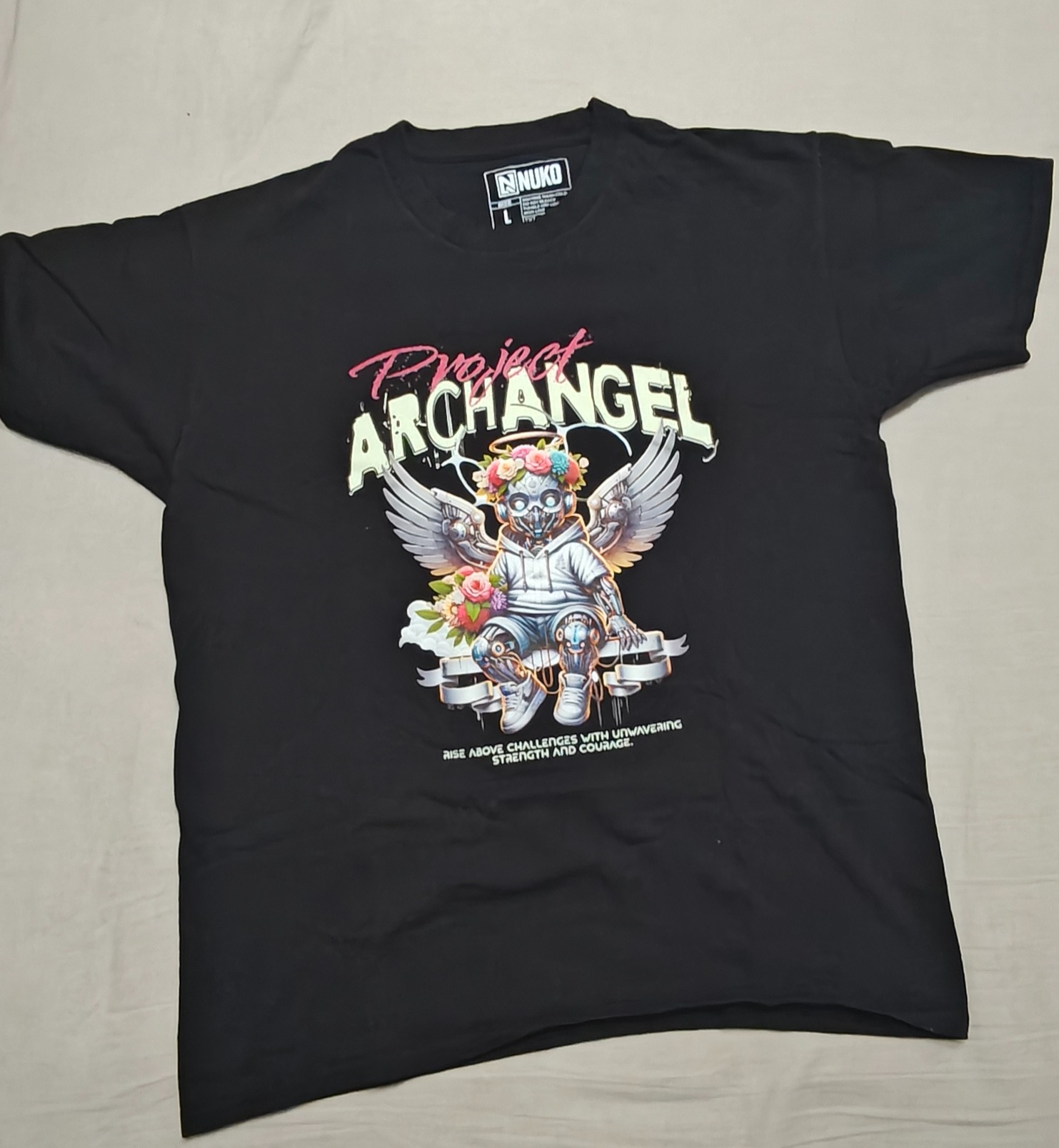Czarna koszulka z nadrukiem 'Project Archangel', przedstawiającym futurystycznego anioła z kwiatami. Widoczne logo 'NUKO' i napis 'Rise above challenges...'.