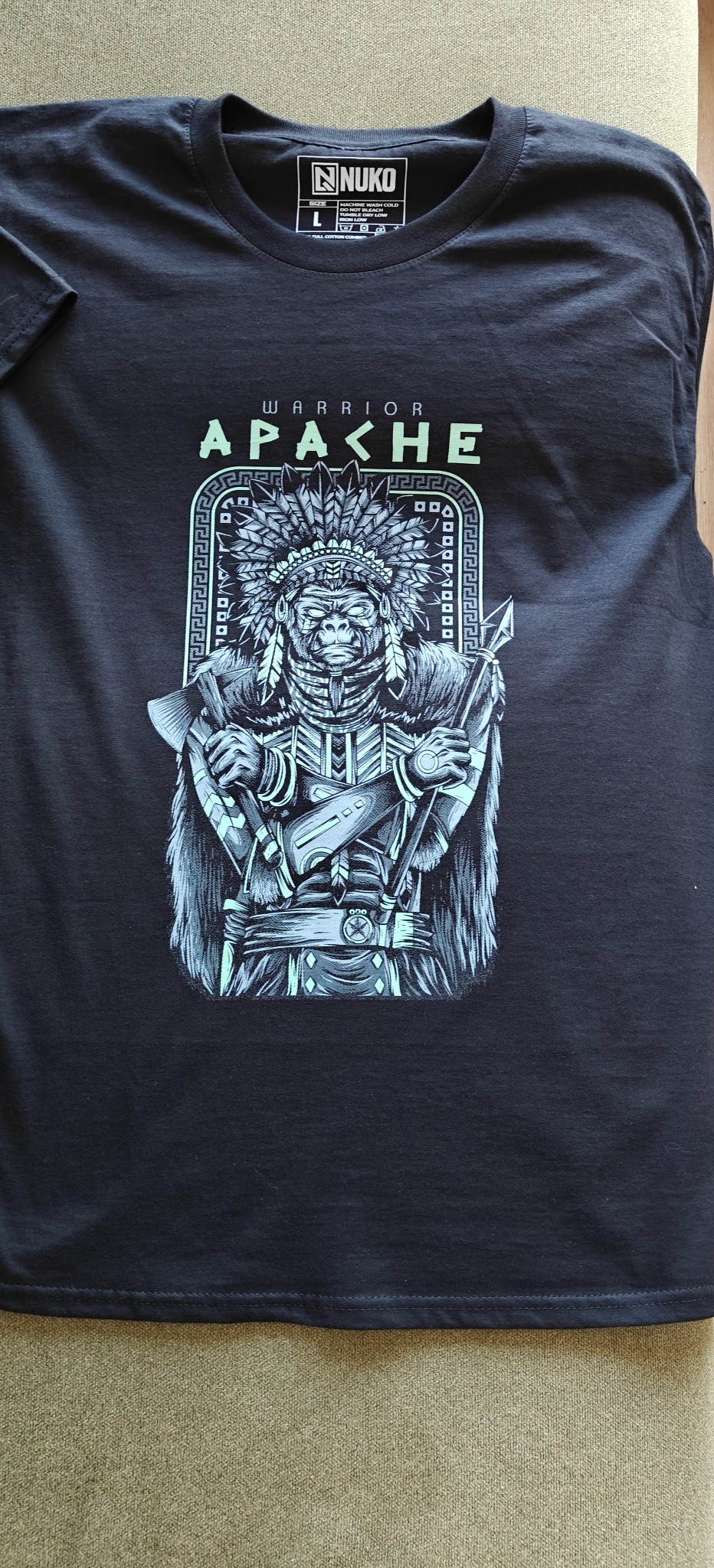 Czarna koszulka z nadrukiem goryla w stroju wojownika Apache, leżąca na płaskiej powierzchni. Widoczna metka marki 'NUKO'.