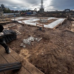Usługi Remontowo-Budowlane Piotr Furtak - Zalane fundamenty domu jednorodzinnego, widoczne zbrojenia i szalunki. W tle dźwig budowlany i zabudowa jednorodzinna. Pochmurne niebo.