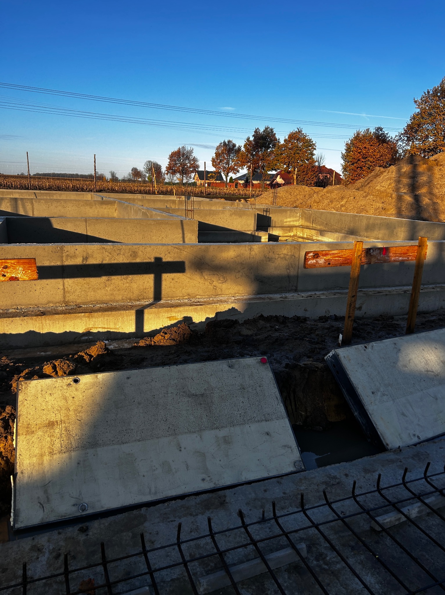 Zalane fundamenty domu jednorodzinnego w surowym stanie, widoczne szalunki i zbrojenia, ziemia, błękitne niebo w tle. Ujęcie z dołu, wczesne popołudnie.
