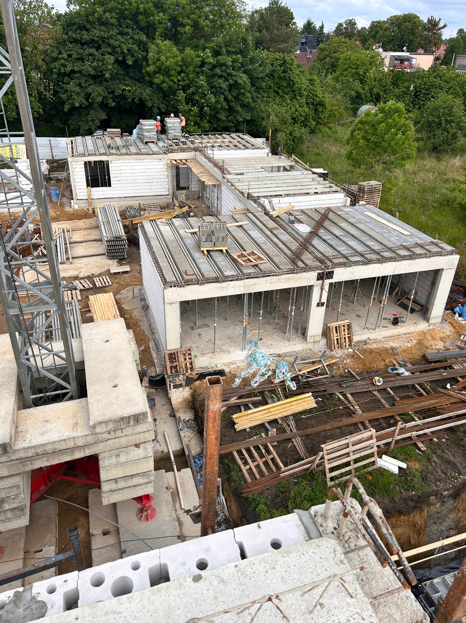 Budowa domu jednorodzinnego z betonu komórkowego: ściany, strop Teriva, zbrojenie. Widok z góry na plac budowy z dźwigiem i pracownikami w oddali.