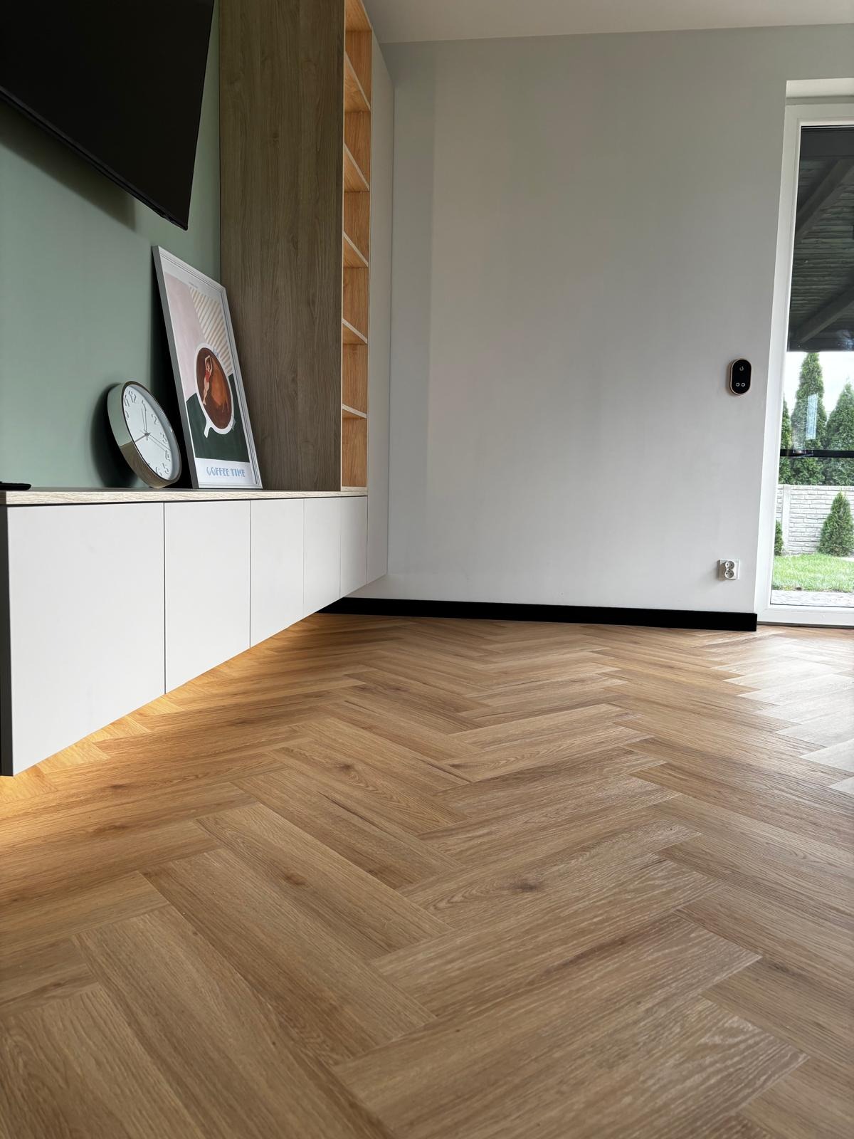 Jasna podłoga z paneli ułożonych w jodełkę francuską, w nowoczesnym wnętrzu z zieloną ścianą, białymi szafkami i minimalistycznym wystrojem. Widok z niskiej perspektywy.