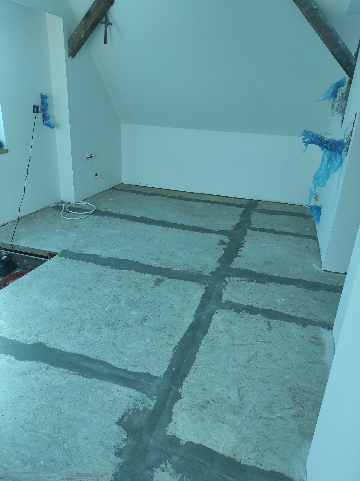 Przygotowanie podłoża pod panele na poddaszu: płyty OSB z uszczelnionymi szczelinami dylatacyjnymi. Widoczne zabezpieczone instalacje i elementy konstrukcyjne dachu.