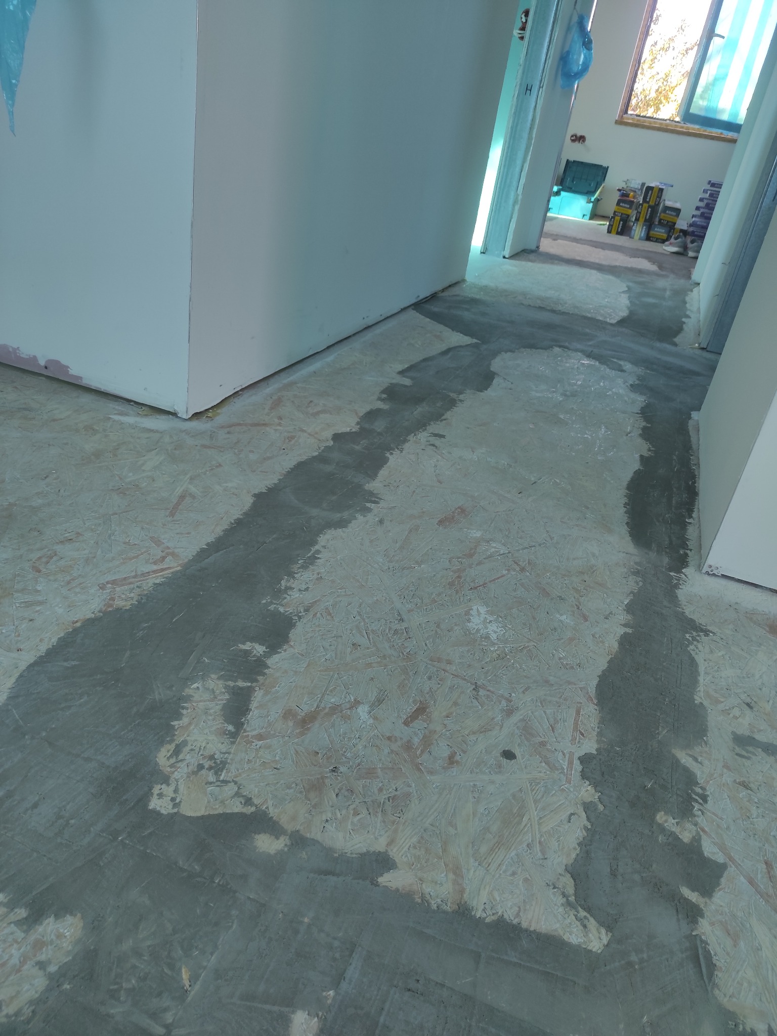 Przygotowanie podłoża pod panele: gruntowanie płyty OSB w pomieszczeniu z widocznymi puszkami farb w tle. Kątowe ujęcie, surowy stan wykończenia.