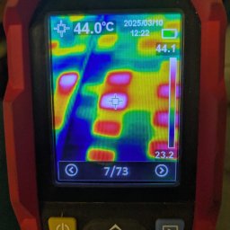 EkoSprzęt Filip Grygo - Kamera termowizyjna w czerwonej obudowie, wyświetlająca rozkład temperatur na ekranie. Widoczne wartości temperatur i data 2025/03/10. Prezentacja testu termicznego instalacji.
