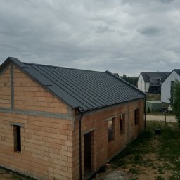 ZAKŁAD OGÓLNOBUDOWLANY RADOSŁAW DUDZIAK - Surowy budynek z szarym dachem z blachy na tle pochmurnego nieba. Widoczne rynny i ceglana konstrukcja w stanie surowym otwartym.