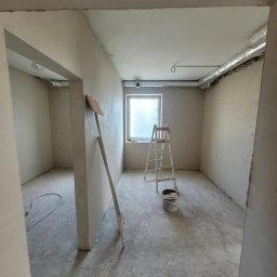 Tynki maszynowe Paweł - Pokój po nałożeniu gładzi, widoczna drabina, wiadro i narzędzie oparta o ścianę. Ściany i sufit pokryte świeżą, jasną gładzią. Widok z perspektywy wejścia.